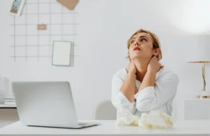 Mujer sentada frente a un ordenador con gesto de cansancio, mostrando signos de estrés, representando la necesidad de tratamiento con un psicólogo online en Badajoz.