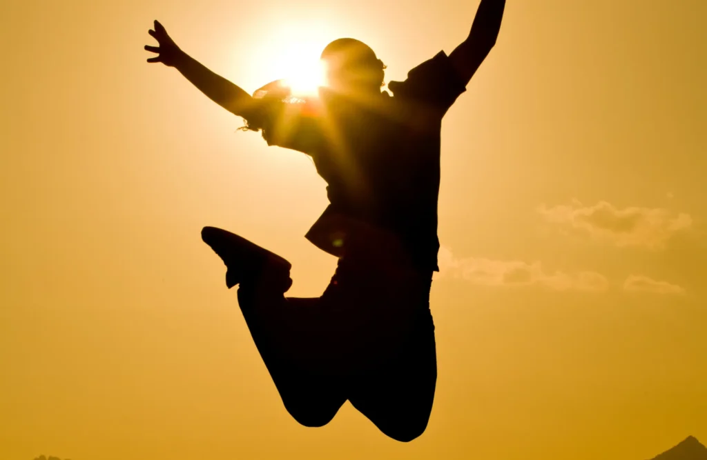 Silueta de una persona saltando de alegría con el sol de fondo, simbolizando el éxito y la felicidad alcanzados a través de la terapia online en Alicante.