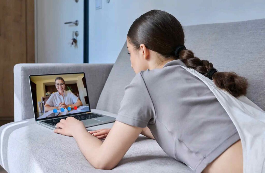 Joven participando en una sesión de psicología online, recostada en el sofá con una computadora portátil mostrando una videollamada con su psicóloga. Esta imagen ilustra el acceso cómodo y flexible a servicios de salud mental desde cualquier lugar, destacando la importancia de la terapia online en Málaga.