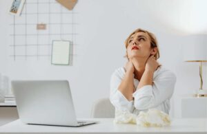 Mujer sentada frente a un ordenador con gesto de cansancio, mostrando signos de estrés, representando la necesidad de tratamiento con un psicólogo online en Málaga.