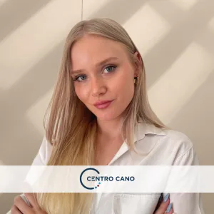 Carol Andersson, psicóloga en línea del Centro Cano, con cabello rubio largo, vestida con una blusa blanca, con los brazos cruzados y una expresión segura y profesional.