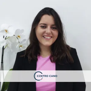 Irene García, psicóloga en línea del Centro Cano, sonriendo, vestida con una chaqueta oscura y una camiseta rosa, con una planta de orquídeas blanca en el fond