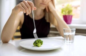 Mujer con signos de trastorno alimentario, mirando desmotivada un plato con comida. Apoyo psicológico online en Cáceres para tratar trastornos de la alimentación y promover la recuperación y el bienestar emocional.